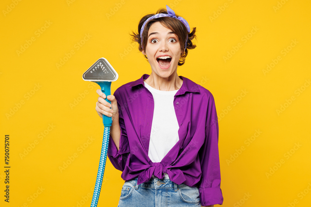 Young shocked surprised woman wears purple shirt casual clothes do housework tidy up hold in hand steamer look camera isolated on plain yellow color background studio portrait. Housekeeping concept. - obrazy, fototapety, plakaty 