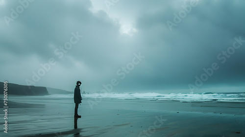 A moody image of a boy standing alone on a deserted beach  surrounded by vast ocean waves  listening to music through his headphones   