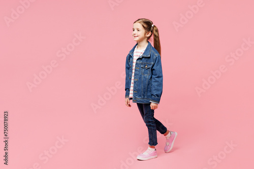 Full body side view little child smiling cute kid girl 7-8 years old wears denim shirt have fun walking go isolated on plain pastel light pink background. Mother's Day love family lifestyle concept
