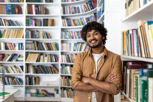 Obraz na płótnie A cheerful young man with curly hair stands confidently with his arms crossed in a well-stocked library