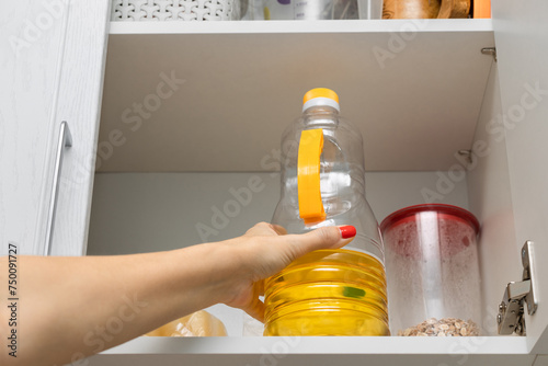  the housewife takes out a bottle of sunflower oil from the kitchen cabinet.