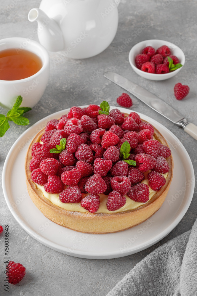 Delicious raspberry tart with vanilla custard cream sprinkled with powdered sugar on a white plate on a gray concrete background. Summer dessert. Delicious raspberry tart with vanilla custard cream sprinkled with powdered sugar on a white plate on a gray concrete background. Summer dessert.