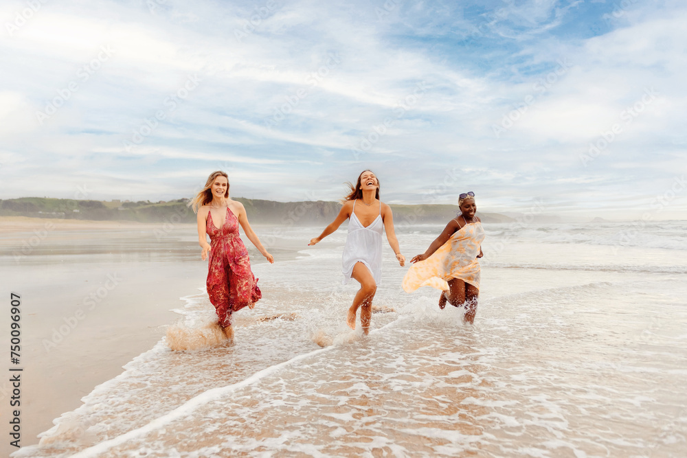 multiracial group of three girls of different races and sizes enjoy running together along the shore of the beach. summer trip among friends.