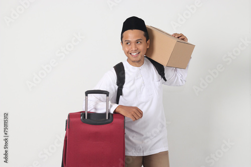 Portrait of excited Asian muslim man in koko shirt with peci carrying cardboard box and holding suitcase. Going home for Eid Mubarak. Isolated image on white background