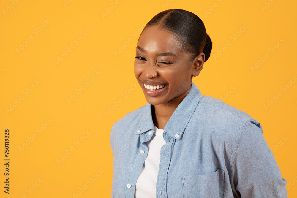 African American lady winks playfully at camera on yellow background African American lady winks playfully at camera on yellow background