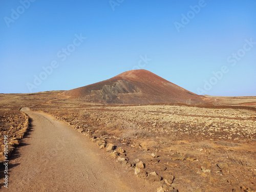 Dirt road in desert landscape with volcano on the horizon under blue sky. Nature and extreme sports.