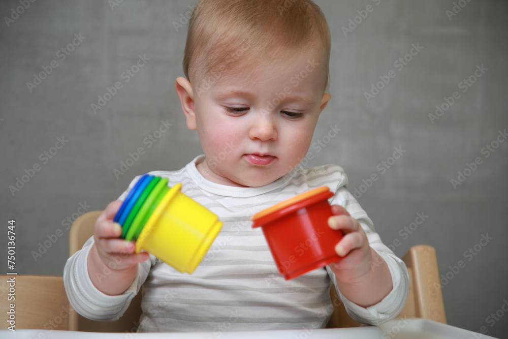 10 months baby girl playing with colorful plastic toy elements on a neutral grey background: Concept of development, play, growth, attention 10 months baby girl playing with colorful plastic toy elements on a neutral grey background: Concept of development, play, growth, attention