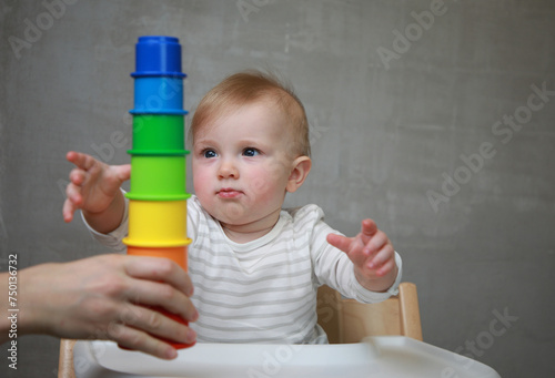 10 months baby girl pulls hands toward colorful pyramid toy to play with it: Concept of play, interaction, development, growth