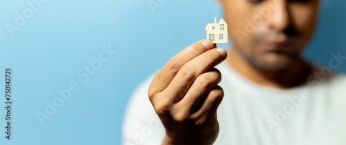 A young person holding a model of a wooden house against a light blue background in the foreground. copyspace