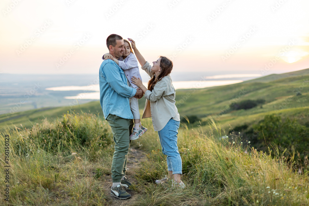 Happy family concept . Little girl is sitting on her father's shoulders, lake on the background. Young mother carries her baby girl daughter at sunset. Family holiday in nature. Happy family concept . Little girl is sitting on her father's shoulders, lake on the background. Young mother carries her baby girl daughter at sunset. Family holiday in nature.
