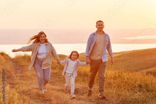 Happy family: mother father and child daughter run on nature on sunset. Summer concept. People spend time outdoor in summer