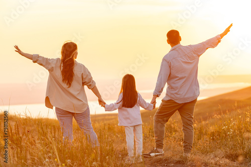 Happy family: mother father and child daughter on nature on sunset. Mom, dad and child are happy walking at sunset. The concept of a happy family. Parents hold the child's hands.