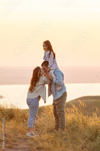 Happy family: mother father and child daughter on nature on sunset. The child sits on his father's shoulders. Summer concept. People spend time outdoor in summer
