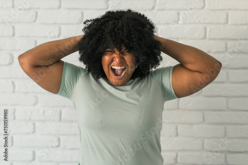 Angry african american woman screaming on brick background. Bad aggressive emotions and premenstrual syndrome or pms concept photo