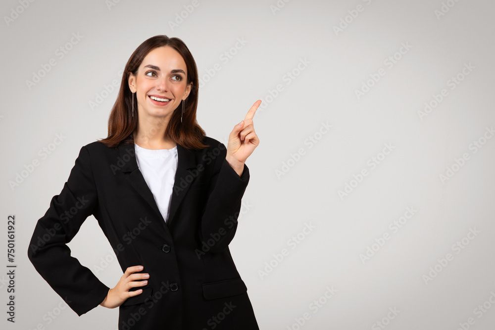 Optimistic businesswoman with a beaming smile, wearing a black blazer, casually pointing upwards Optimistic businesswoman with a beaming smile, wearing a black blazer, casually pointing upwards