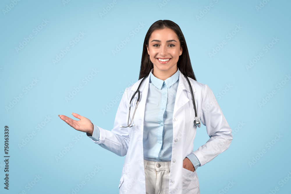Smiling woman doctor presenting something with hand on blue backdrop Smiling woman doctor presenting something with hand on blue backdrop