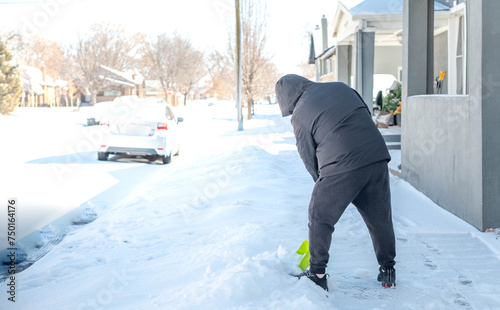 A man in a warm black jacket and trousers shoveling snow in front of their home for prepare the road for convenience. photo