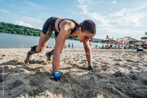 Female athlete doing pushups on a sandy beach during obstacle course race