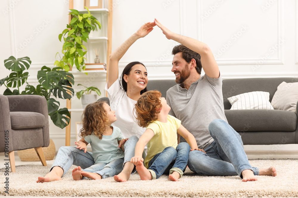 Family housing concept. Happy woman and her husband forming roof with their hands while sitting with kids on floor at home Family housing concept. Happy woman and her husband forming roof with their hands while sitting with kids on floor at home