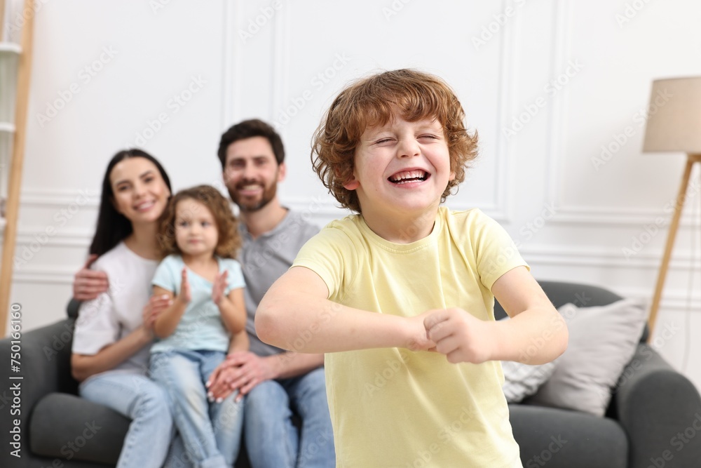 Happy family having fun at home. Son dancing while his relatives resting on sofa