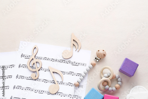 Wooden notes, music sheets and toys on beige background, flat lay with space for text. Baby song concept