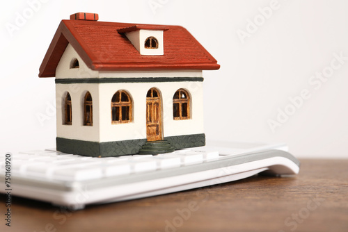 Mortgage concept. House model and calculator on wooden table against white background, closeup