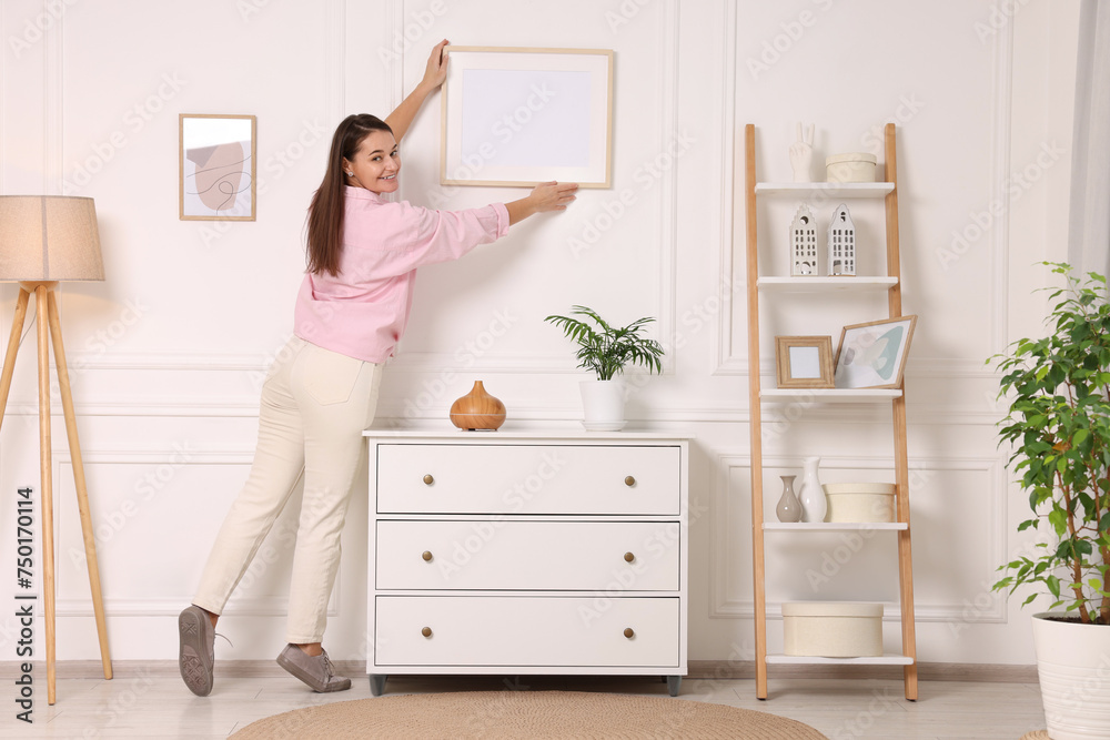 Woman hanging picture frame on white wall at home
