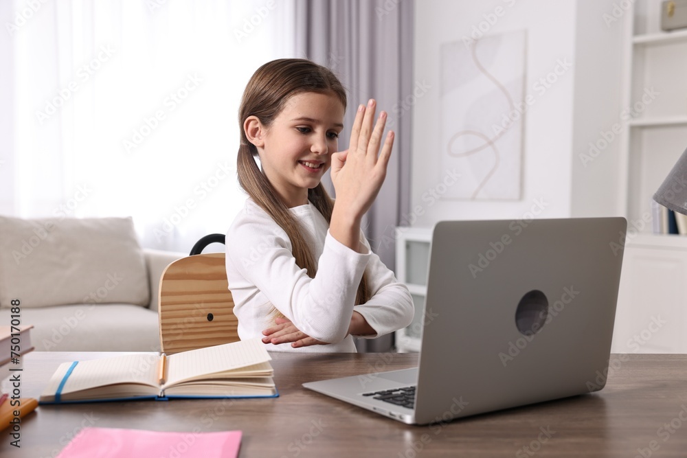 E-learning. Cute girl raising her hand to answer during online lesson at table indoors E-learning. Cute girl raising her hand to answer during online lesson at table indoors