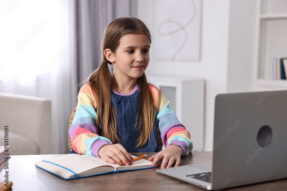 E-learning. Cute girl using laptop during online lesson at table indoors E-learning. Cute girl using laptop during online lesson at table indoors