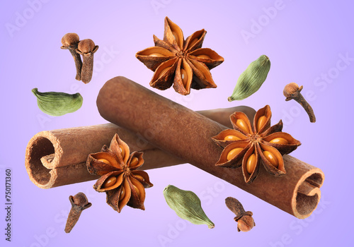 Cinnamon stick and other aromatic spices falling on violet background