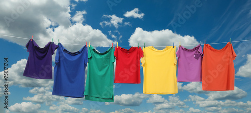 Colorful t-shirts drying on washing line against blue sky, banner design