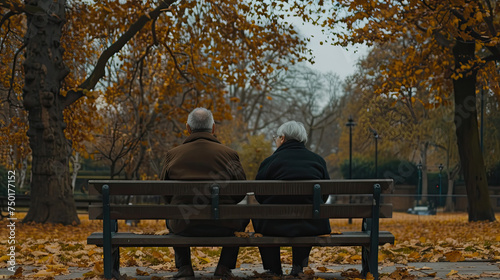 Two individuals are seated on a bench in a park, surrounded by greenery. They appear relaxed and engaged in conversation as they enjoy the outdoors