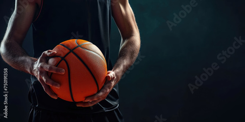 A basketball player in a dark setting holds the ball with determination, preparing for the game ahead.