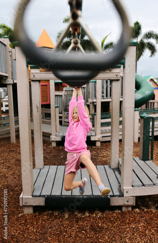 Happy Little Girl Child Swinging on Monkey Bar Rings at Playground