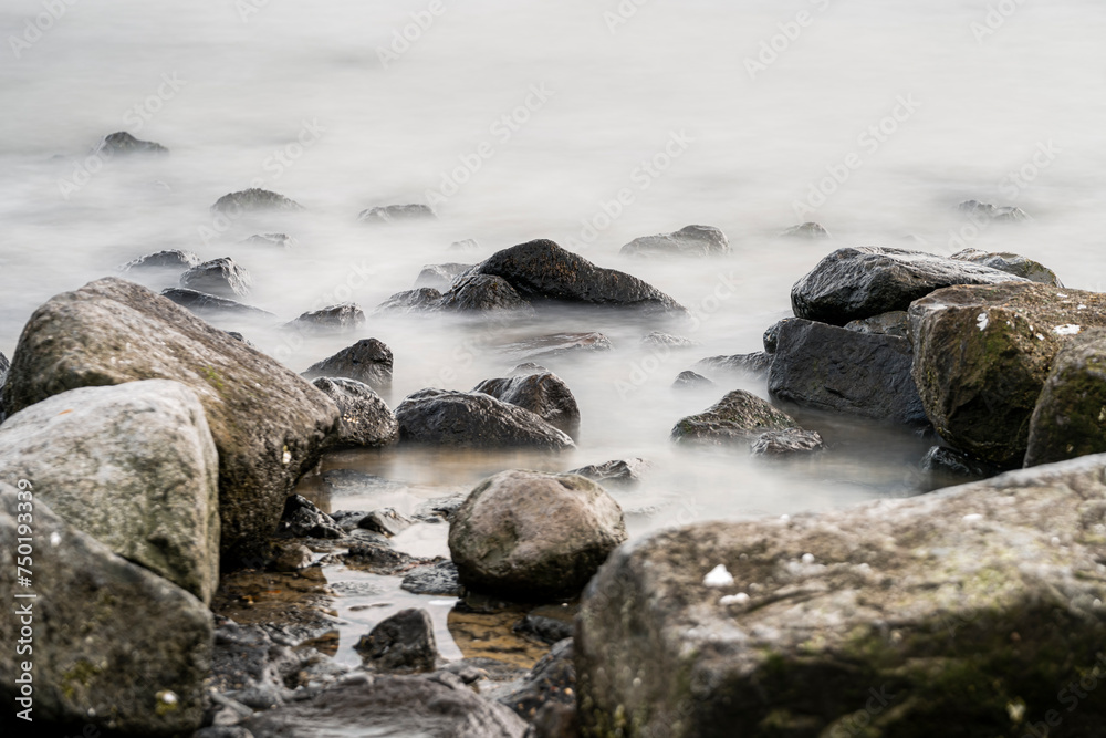 Obraz premium Picturesque view of rough rocky formations in foamy seawater with mossy round boulders near coast
