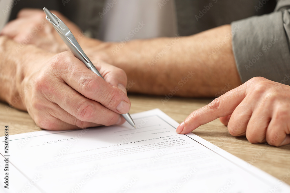 Notary pointing to senior man where to sign Last Will and Testament at wooden table, closeup Notary pointing to senior man where to sign Last Will and Testament at wooden table, closeup