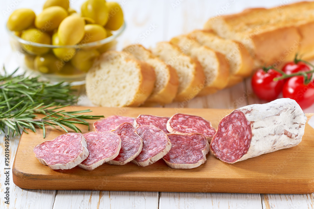 Slices of pork dry cured salami sausage and slices baguette on a wooden table. Slices of pork dry cured salami sausage and slices baguette on a wooden table.