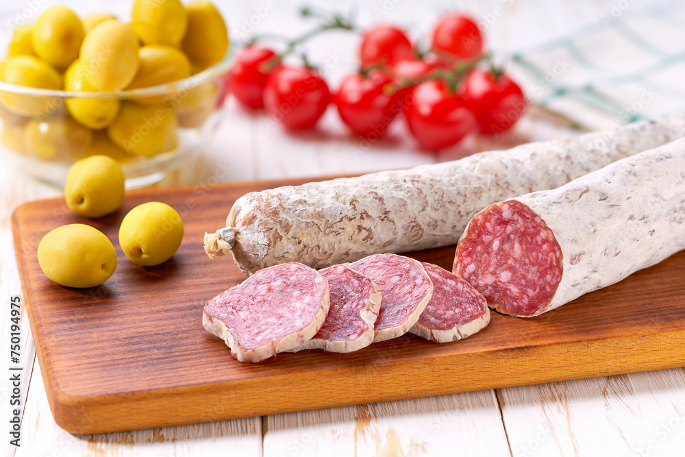 traditional Spanish salami fuet sausage with rosemary and baguet on a cutting board close up. traditional Spanish salami fuet sausage with rosemary and baguet on a cutting board close up.