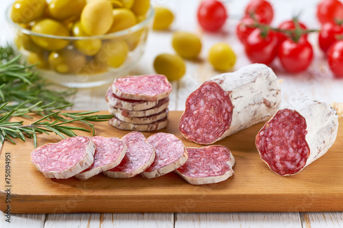 Spanish Fuet sausage salami with rosemary and olives on a wooden cutting board.