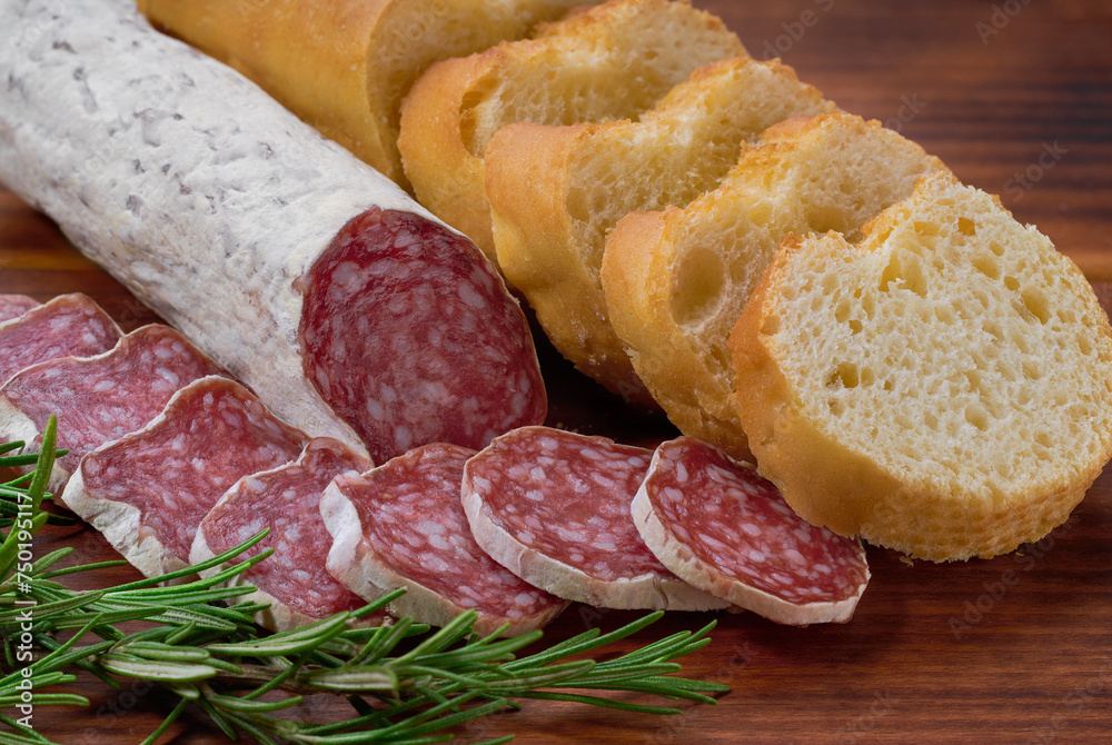 Spanish Fuet sausage salami with rosemary and french baguette on a cutting board.