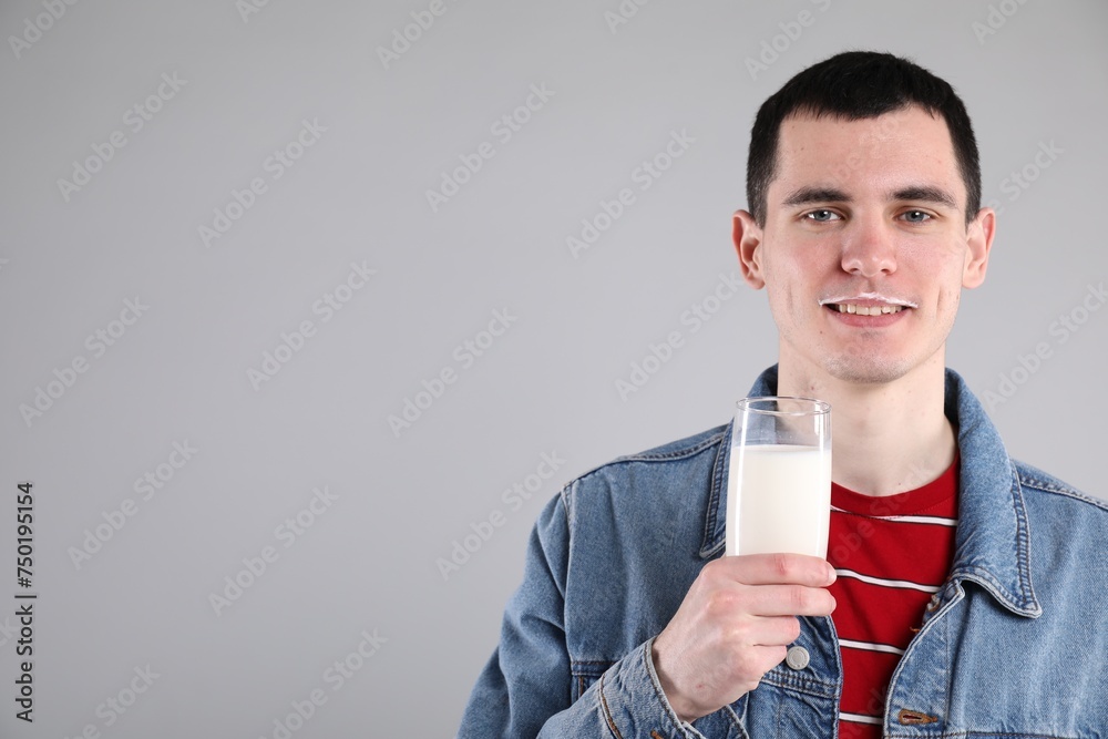 Happy man with milk mustache holding glass of tasty dairy drink on gray background, space for text Happy man with milk mustache holding glass of tasty dairy drink on gray background, space for text