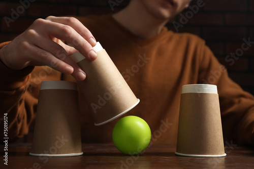 Photography Shell game. Man showing ball under cup at wooden table, closeup