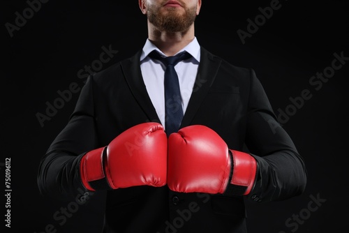 Businessman in suit wearing boxing gloves on black background, closeup © New Africa