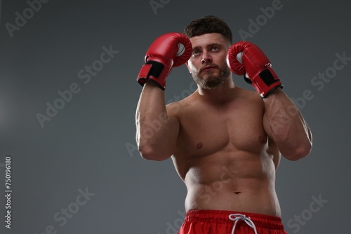 Man in boxing gloves on grey background, low angle view. Space for text