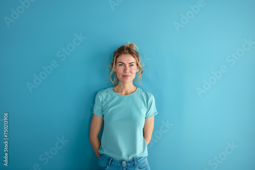 Woman in her thirties wearing a blue t-shirt and standing in front of blue wall with her hands behind her back