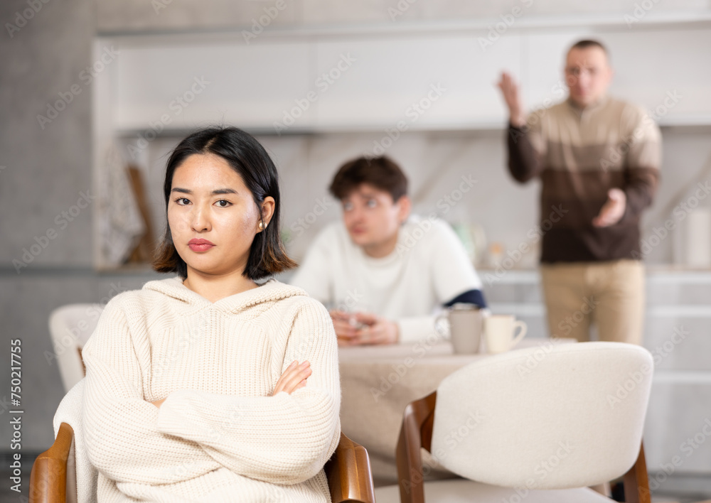 Upset young woman not talking after disagreement with father and husband standing behind