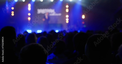 The view from the auditorium, on a concert stage with a professional stage light in blue tones, a speaker on personal growth or success speaks. Unrecognizable faces. High quality 4k footage photo