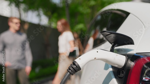 Focused EV electric car charging in green sustainable city outdoor garden in summer show lifestyle on blur background of young couple in urban green sustainable rechargeable electric vehicle innards