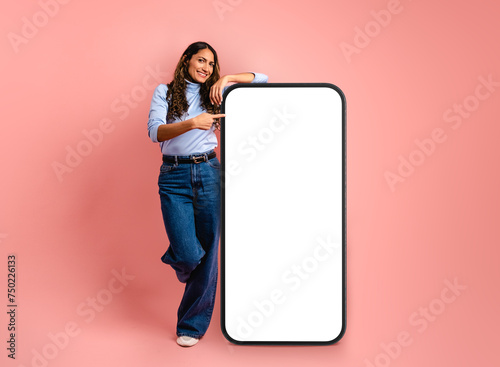 Smiling adult Colombian woman demonstrating smartphone against pink background