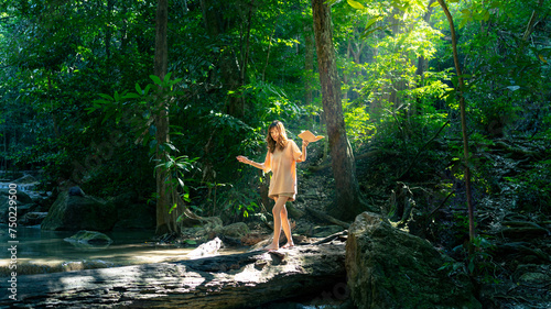 Happy young Asian woman enjoy and fun outdoor lifestyle travel nature forest mountain on summer holiday vacation. Attractive girl walking on tree trunk over lagoon at tropical forest waterfall.